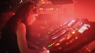 Photo of a young DJ with a controller in a red-lit club 
