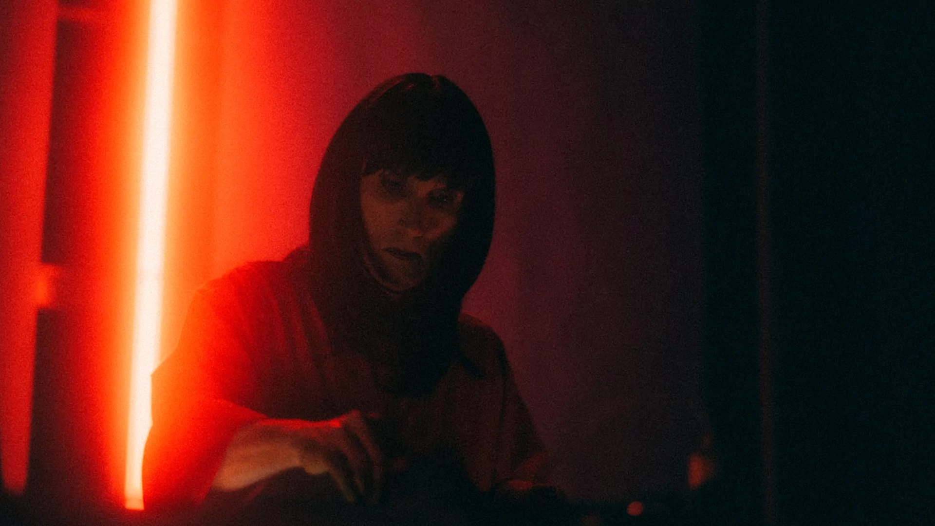 Photo of Rrose DJing in a dark club with a red strip light behind them